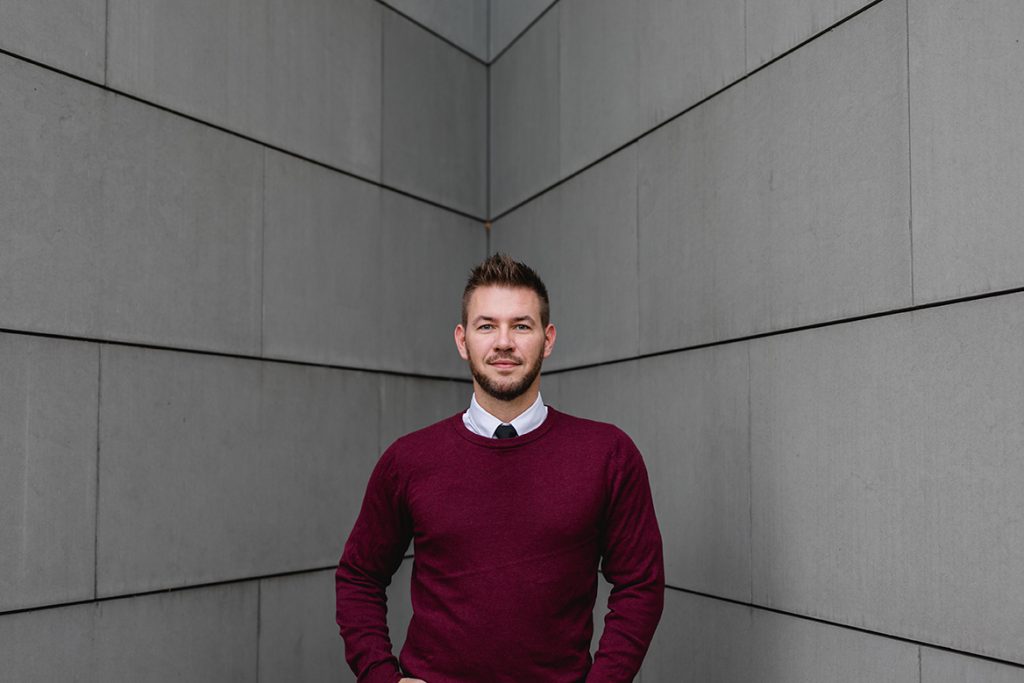 Businessportrait eine Mannes vor grauen Platten im roten Pullover - Fotografin: Sonja Yasmin Fotografie, Hochzeitsfotografin in Köln, Bonn und ganz NRW, Fotografin für Portraitfotos und Familienfotos