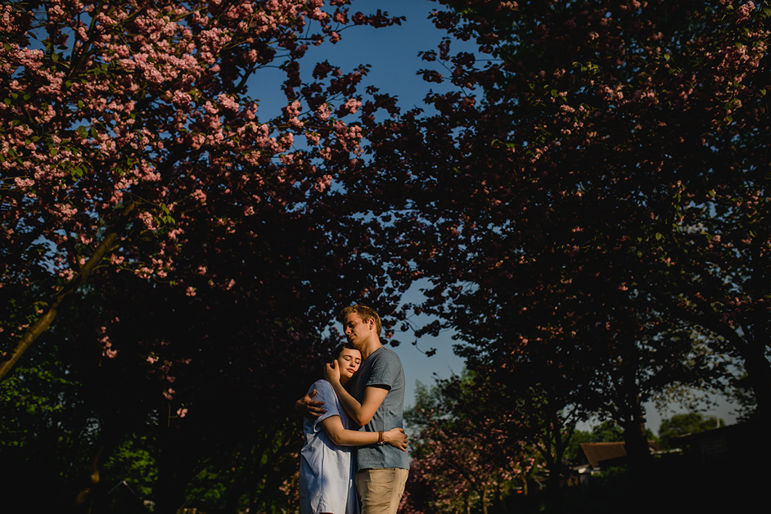 Das Paar hält sich in den Armen vor blauem Himmel und Kirschblüten - Fotografin: Sonja Yasmin Fotografie, Hochzeitsfotografin in Köln, Bonn und ganz NRW, Fotografin für Portraitfotos und Familienfotos