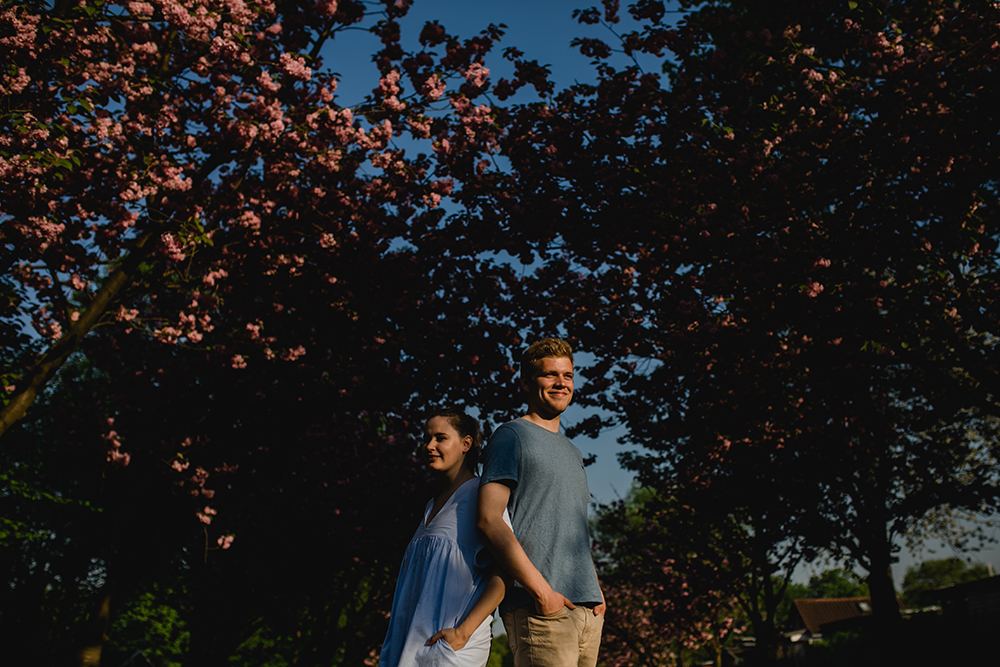 Das Paar Rücken an Rücken vor blauem Himmel und Kirschblüten - Fotografin: Sonja Yasmin Fotografie, Hochzeitsfotografin in Köln, Bonn und ganz NRW, Fotografin für Portraitfotos und Familienfotos