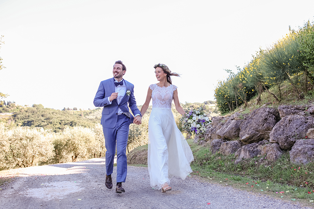 Braut und Bräutigam laufen einen Weg entlang auf ihrer Hochzeit in der Toskana. Im Hintergrund Olivenbäume - Fotografin: Sonja Yasmin Fotografie, Hochzeitsfotografin in Köln, Bonn und ganz NRW, Fotografin für Portraitfotos und Familienfotos