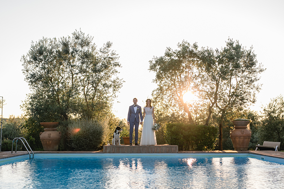 Braut und Bräutigam stehen am Pool mit Hund in der Toskana beim Sonnenuntergang während des Brautpaarshootings - Fotografin: Sonja Yasmin Fotografie, Hochzeitsfotografin in Köln, Bonn und ganz NRW, Fotografin für Portraitfotos und Familienfotos