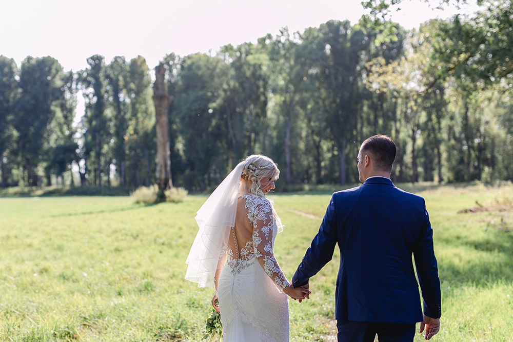 Das Brautpaar geht in Brautkleid und Anzug Hand in Hand über die Wiese während des Paarshootings - Fotografin: Sonja Yasmin Fotografie, Hochzeitsfotografin in Köln, Bonn und ganz NRW, Fotografin für Portraitfotos und Familienfotos