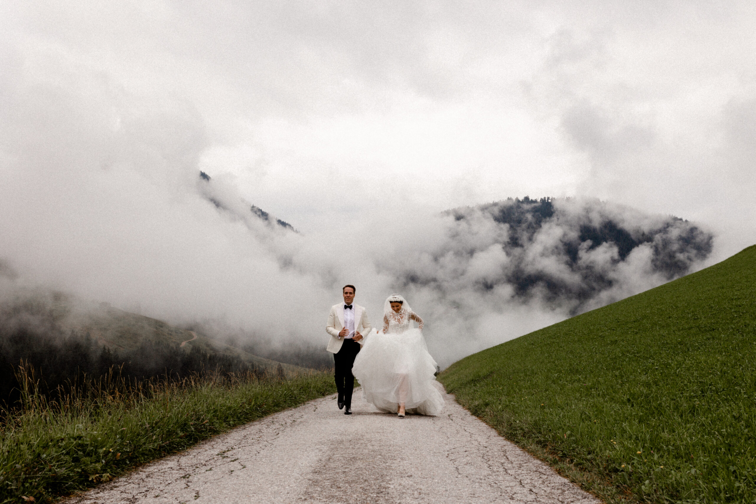 Das Brautpaar vor den Bergen und dem Nebel auf dem Weg während des Paarshootings Ein tolles Naturschauspiel in Südtirol während der Destinationwedding - Fotografie NRW Köln Bonn Wesseling
