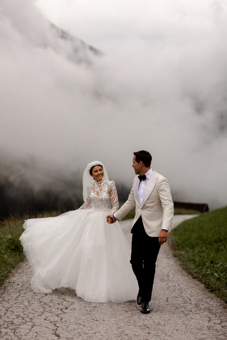 Die strahlende Braut an der Hand von ihrem coolen Ehemann vor dem Nebel in den Bergen in Südtirol. Sie trägt ein traumhaftes Brautkleid und trägt einen stylischen Smoking - Fotografin: Sonja Yasmin Fotografie, Hochzeitsfotografin in Köln, Bonn und ganz NRW"